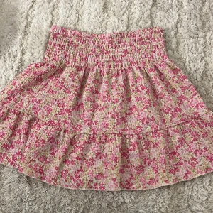 Blommig volangkjol från Gina Tricot - Supersöt kort volangkjol från Gina Tricot med blommigt mönster i rosa, vitt och grönt. Kjolen har smock i midjan och är gjord i ett lätt och luftigt material, perfekt för varma dagar. Passar dig som gillar en feminin och somrig stil. Inga defekter 💞