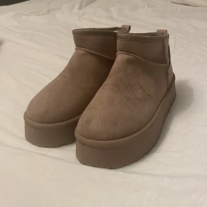 Beige Platå ”UGG” - Chunky beige platå UGG imitation. Dom är helt oanvända. Utsidan är i mjuk mockaliknande syntet och insidan är fodrad med vit fuskpäls för extra värme. Perfekta för kalla dagar och ger en cool vibe till din outfit.