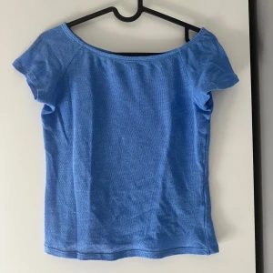 Blå topp från Monki - Säljer en ljusblå topp från Monki med korta ärmar och bred, något båtformad halsringning. Toppen är i mjukt material och har en enkel, stilren design som passar perfekt till jeans eller kjol.