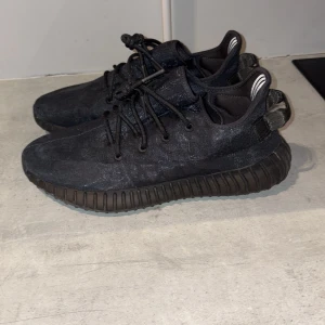 Yeezy Boost 350 V2 Mono Cinder sneakers - Säljer ett par svarta Adidas Yeezy Boost 350 V2 sneakers med stickad ovandel, svarta snören och klassisk ribbad sula. Skorna har diskreta ränder och orange innersula med Yeezy-tryck.