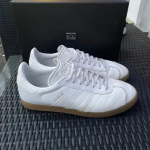 Vita Adidas Gazelle sneakers - Snygga vita Adidas Gazelle sneakers i bra skick storlek 43, passar bra med de mesta. Skriv vid eventuella frågor 😀