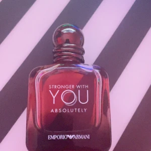  Stronger With You absolutely  - Ca 45ml kvar. Emporio Armani Stronger With You Absolutely är en parfym i en stilren, fyrkantig glasflaska med mörkröd och bärnstensfärgad ton. Flaskan har rundad kork och tydlig logga framtill. Doften är intensiv och modern, perfekt för dig som gillar exklusiva och djärva parfymer.