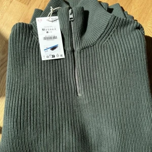 Mörkgrön stickad half zip-tröja M - Säljer en mörkgrön stickad tröja från Uniqlo i storlek M. Tröjan har en ribbad struktur, hög krage och half zip-dragkedja framtill. Perfekt för lager-på-lager och chill stil. Långärmad och riktigt skön.