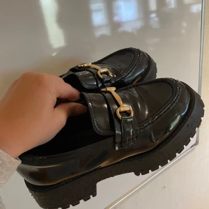 Loafers - Glansiga loafers med gulddetalj. Väldigt sköna att gå i, använda ett fåtal gånger. Mycket bra skick.