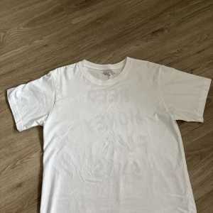 Vit t-shirt med tryck 'Need Money For Snus' - Vit t-shirt från GOT i bomull med svart tryck på ryggen där det står 'Need Money For Snus' i en cool, droppande font. Klassisk passform med rund hals och korta ärmar. Perfekt statement-plagg för dig som gillar humor och streetstyle.