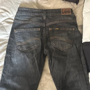  Barnjeans Mörkgrå Lee jeans W24 L31 - Snygga mörkgrå jeans från Lee till barn med klassisk femficksdesign och kontrastsömmar. Jeansen har låg midja och raka ben, tillverkade i bomull med en skön känsla. Perfekta för dig som gillar en tidlös och avslappnad look.
