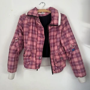 Rutig rosa jacka med dragkedja - Säljer en cool rutig jacka i rosa och lila nyanser. Jackan har dragkedja och knappar framtill, samt ribbade muddar vid ärmslut och nederkant. Den har praktiska fickor och en dekorativ detalj på ärmen. Färgen syns bäst på bild 2 och 3💫✨💕 står strl XL på tagen men passar S! Obs Dragkedjan är trasig men har också knappar