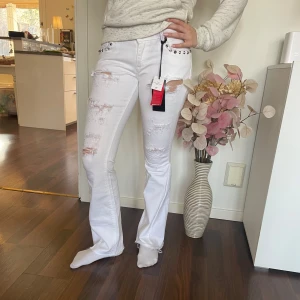 Vita jeans med nitar och slitningar - Fina och trendiga vita bootcut jenas, med låg midja och nitar i fram. De är omsydda till bootcut, men det syns inte mycket då det är vitt. Tjejen på bilden är 158 cm och har ofta storlek XS, byxorna sitter lite tajt💗💗