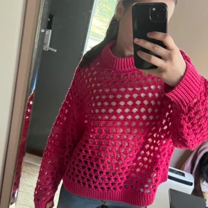 Rosa stickad oversized tröja - Säljer en snygg rosa stickad tröja med ett öppet mönster. Tröjan har långa ärmar och ribbade muddar vid ärmslut och nederkant. Perfekt för lager-på-lager-stil. Passar bra till jeans eller kjol för en avslappnad look. 