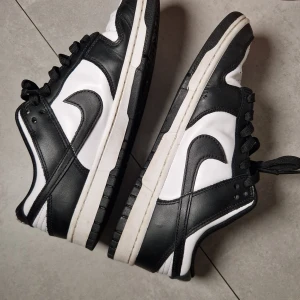 Svartvita Nike Dunk sneakers - Panda storlek 42,5 - Snygga svartvita Nike Dunk sneakers med klassisk design. Skorna har en stilren svart och vit färgkombination med snörning och den ikoniska Nike-loggan på sidan. Perfekta för en sportig och trendig look. Väldigt sparsamt använda och nästan nyskick.