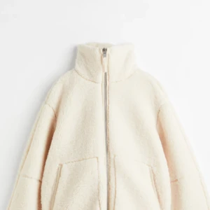 Vit teddyjacka med dragkedja - Mysig vit teddyjacka med dragkedja och hög krage. Perfekt för kyliga dagar med sin fluffiga och varma design. Jackan har långa ärmar och praktiska fickor framtill.