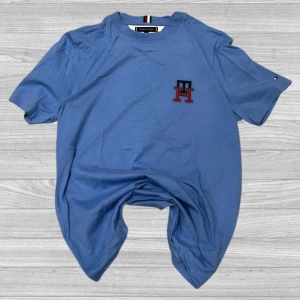 Tommy Hilfiger T-Shirt - Snygg blå t-shirt från Tommy Hilfiger med broderad TH-logga i rött och blått på bröstet. T-shirten har korta ärmar och en klassisk rund halsringning. Perfekt för en avslappnad stil.