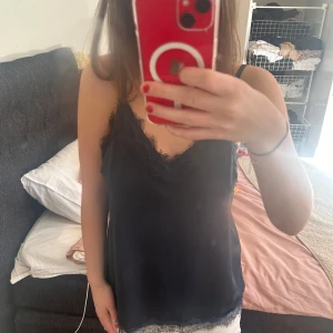 mörkblått linne med spetsdetaljer - vacker mörkblått med tunna axelband och vacker spetskant vid halsringning och nederkant. Perfekt för en stilren och elegant look.