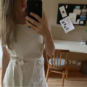 Vit ärmlös klänning med knytband - Säljer en söt vit ärmlös klänning med knytband i midjan. Klänningen har en volangdetalj längst ner och är perfekt för varma dagar. Enkel och stilren design som passar till många tillfällen.