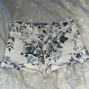 Blommiga shorts från H&M - Snygga vita shorts med blått blommönster från H&M. De har en knapp och dragkedja framtill samt praktiska fickor både fram och bak. Perfekta för en somrig look!
