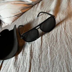 Svarta solglasögon - Snygga svarta solglasögon med en klassisk design. De har en rektangulär form och en solid svart båge. Perfekta för soliga dagar och ger en stilren look.