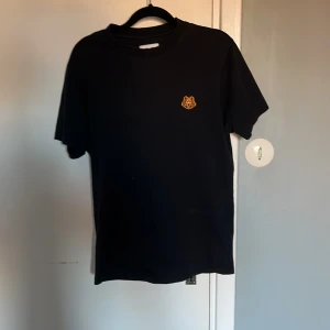 Svart t-shirt från Kenzo - Säljer en stilren svart t-shirt från Kenzo med ett broderat tigeremblem på bröstet. T-shirten är kortärmad och gjord i mjuk bomull. 