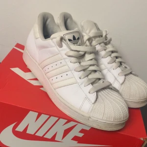 Vita sneakers från Adidas - Klassiska vita sneakers från Adidas med de ikoniska tre ränderna på sidan. Skorna har snörning och en rund tå. Perfekta för en stilren och sportig look.