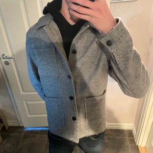 Grå overshirt från Lindbergh - Säljer en stilren grå overshirt från Lindbergh i storlek M. Jackan har en klassisk krage och knäppning framtill med svarta knappar. Två stora fickor framtill ger en cool look. Perfekt för lager-på-lager-stil. Hör av vid funderingar och frågor!!
