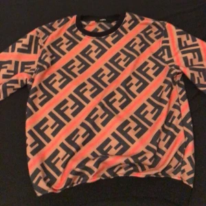 Mönstrad tröja från Fendi - Säljer en snygg tröja från Fendi med ett iögonfallande mönster i svart, beige och rött. Tröjan har långa ärmar och en rund halsringning. Perfekt för dig som vill sticka ut med stil!