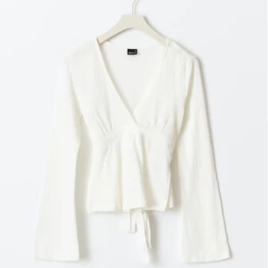 Tie top - Texturerad topp med knytning bak. Toppen är vit och har v-ringning. Den har normal passform, utsvängd ärm och rynkningar under bysten. Från Gina tricot