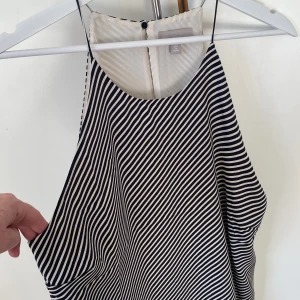 Randigt helfodrat linne med smala axelband - Tunnt och helfodrat linne med smala axelband och diagonala ränder i svart och off white. Knäppning i nacken och väldigt fint fall. Längd 70 cm. Storlek M. Aldrig använt. 