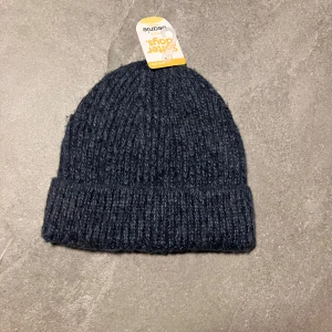 Marinblå stickad mössa  - Snygg och varm marinblå mössa, perfekt för kyliga dagar. Tillverkad i en blandning av polyester och ull för extra komfort och värme. Den ribbade designen ger en klassisk look.