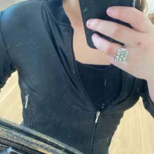 Svart kofta  från Gina Tricot - Snygg svart kofta från Gina Tricot med dragkedja framtill och på fickorna. Koftan har en stilren design och är perfekt för en cool look. Den är tillverkad i ett glansigt material som ger en modern touch.plus❤️❤️