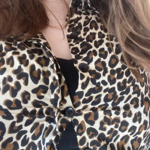 Leopardmönstrad blus med knappar - Snygg leopardmönstrad blus med svarta knappar framtill. Perfekt för att ge en djärv touch till din outfit. Blusen har en klassisk krage och är tillverkad i ett mjukt material.
