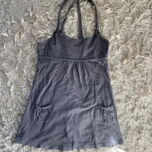Grå klänning med fickor - Säljer en grå miniklänning med knappar vid axelbanden och en lätt rynkad detalj under bysten. Jätte fin men är lite för liten på min byst💕Passar s-xs