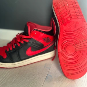 Svart och röd Nike Air Jordans - Säljer ett par klassiska Nike Air Jordans i svart och rött. Skorna har en ikonisk design med snörning och en tydlig Nike-logga på sidan. Perfekta för dig som vill ha en stilren och sportig look.
