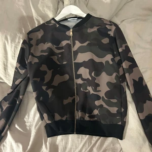 Camouflage bomberjacka från Colloseum - Säljer en snygg camouflage bomberjacka från Colloseum. Jackan har en dragkedja framtill och är långärmad. Perfekt för en cool och avslappnad stil.