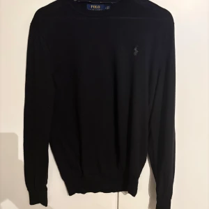 Svart tröja från Polo Ralph Lauren - Säljer en stilren svart tröja från Polo Ralph Lauren i tvättbar merinoull. Tröjan har en slim fit passform och långa ärmar. Perfekt för en elegant och bekväm look.