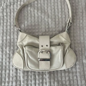 Beige vintage  axelväska med croc-detaljer - Snygg beige vintage  axelväska med croco-präglade detaljer på rem, kanter och spänne. Väskan har en stor ficka framtill med dragkedja och ett coolt metallspänne, samt ytterligare en dragkedjeficka på baksidan. Perfekt storlek för mobilen och det viktigaste. 