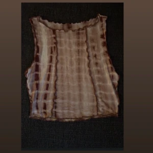 Brun och beige ribbad tubtopp - Säljer en unik ribbad tubtopp i bruna och beige toner med coolt batikmönster. Toppen är ärmlös och har vågiga kanter upptill och nedtill för en trendig look. Perfekt att styla med jeans eller kjol för en fin vibe.