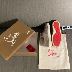 Christian Louboutin - Snygga grå sneakers från Christian Louboutin i mjuk mocka med klassisk röd sula och vita kanter. Skorna har rund tå, snörning och exklusiv känsla. Perfekta för dig som vill sticka ut med lyxiga detaljer och ikonisk design.