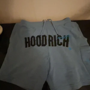 Blå HOODRICH shorts med snörning - Snygga blå shorts från HOODRICH med stor svart logga framtill och coola blå detaljer. Shortsen har snörning i midjan och en praktisk ficka på sidan. Perfekta för chill dagar eller streetwear-stil.