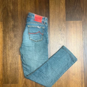 Jacob Cohen 688 Comfort jeans blå - Säljer ett par Jacob Cohën jeans i modell 688, storlek W34. Fina detaljer med röd brodyr på fickorna och rött pälsemblem bak. Lite defekter på märket bak men inget som märks vid användning.  Kvalitetsjeans från italienska Jacob Cohën – kända för sin exklusiva denim och handgjorda känsla.  Längd 101 cm, bredd 42 cm.  Fraktar oftast samma dag!  ✅ Använda men i fint skick ✅ Mjuka och bekväma ✅ Äkta vara  Perfekta för dig som vill ha ett par jeans med premiumkänsla och snygga detaljer!
