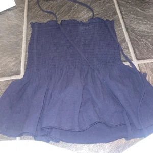 Mörkblå bandeau tubtopp med volang - Supersöt mörkblå bandeau tubtopp med smock upptill och volangig nederdel. Toppen har tunna knytband och är perfekt för varma dagar. Enkel att matcha med jeans eller kjol för en chill look.