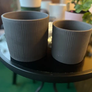 Krukor  - Bilderna visar två grå krukor med räfflad yta, perfekta för inredning eller växter. 