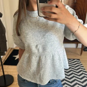 Grå stickad tröja från Nelly - Supermjuk ljusgrå stickad tröja från Nelly med rund halsringning och kortare ärmar. Tröjan har en lätt utsvängd peplumform nedtill. Är som ny och endast använd 1 gång! Säljer för 170kr! Pris kan diskuteras 