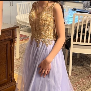 Långklänning med guldpaljetter och tyll - Magisk långklänning med glittrig guldpaljett upptill och lila tyllkjol. Djup v-ringning och ärmlös design ger en elegant look. Perfekt för bal eller fest, med detaljer som sticker ut och ger wow-känsla. Stl S, hade den på mig bara en gång . Jag köpte den för 6000kr säljer den för 1000kr