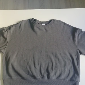 Grå sweatshirt från H&M Divided M - En basic grå sweatshirt från H&M Divided i storlek M. Tröjan har rund halsringning, ribbade muddar och är tillverkad i en mjuk blandning av bomull och polyester. Perfekt för en chill och avslappnad stil. Bara en liten vit fläck men använd max 3 gånger så inprincipt nytt.