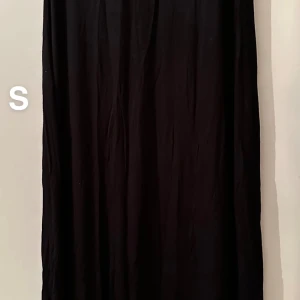 Svart långkjol i bomull, stl S - Enkel och stilren svart långkjol i mjukt bomullstyg. Kjolen har rak passform och faller snyggt längs benen. Perfekt för dig som gillar minimalistisk stil och vill ha en kjol som funkar till många olika looks.🌸Fint använt skick. Storlek s