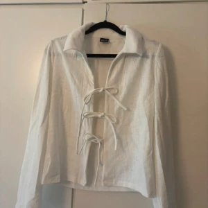 Vit snörad skjorta från Gina Tricot - Vit skjorta från Gina Tricot i storlek XS med snygg snörning framtill. Skjortan har lång ärm, klassisk krage och är tillverkad i ett lätt tyg som känns luftigt. Perfekt för dig som vill ha en unik och trendig look.