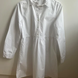 Vit skjortklänning med knappar - Vit skjortklänning med lång ärm och knappar framtill. Avslappnad passform. 