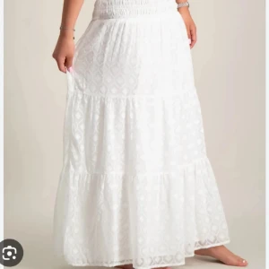 Vit långkjol med volangdetaljer - Superfin vit långkjol med volangdetaljer och diskret mönster. Kjolen har en smockad midja som ger en bekväm passform och ett luftigt fall. Perfekt för varma dagar och ger en romantisk vibe till din outfit.