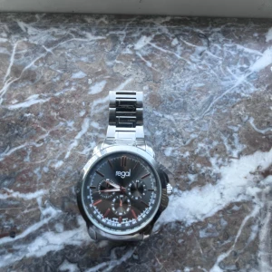 Stilren silverklocka från Regal - Snygg klocka från Regal med svart urtavla och röda detaljer. Klockan har en robust länk i silverfärgat metall och flera små urtavlor för extra funktioner. Perfekt accessoar för dig som gillar en klassisk men modern look.