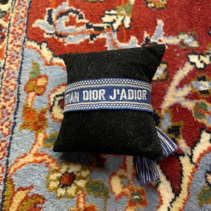Blått Christian Dior J'Adior armband - Snyggt blått tygarmband från Christian Dior med texten 'J'Adior' broderad i vitt. Armbandet har justerbar knytning med tofsar i ändarna och coola detaljer i vitt och blått. Perfekt accessoar för att lyfta din outfit med en lyxig touch. Passar med nästan alla outfits. Riktigt grisch🤛 Pris kan diskuteras