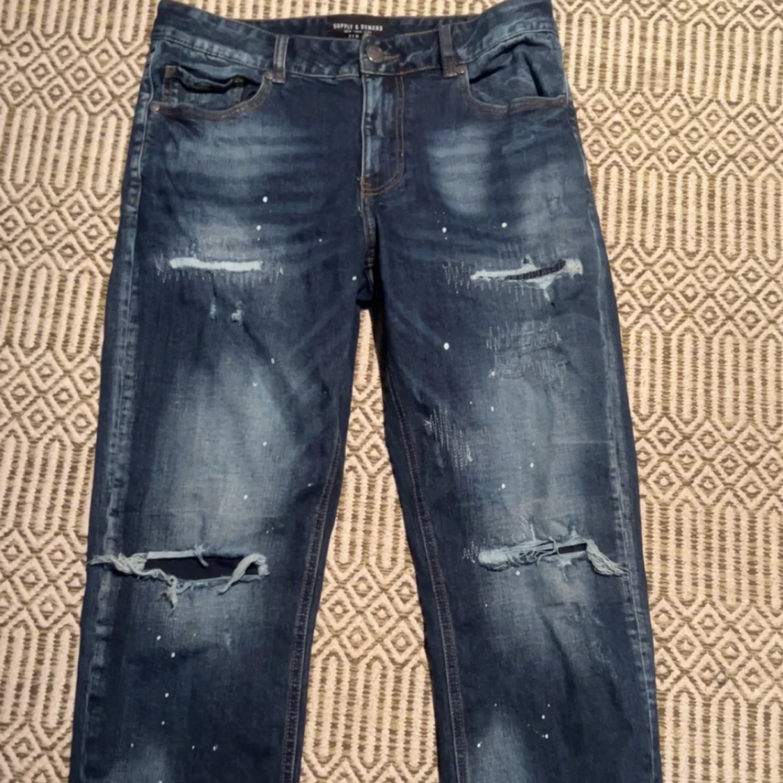 Blå slitna jeans med hål från supply and demand